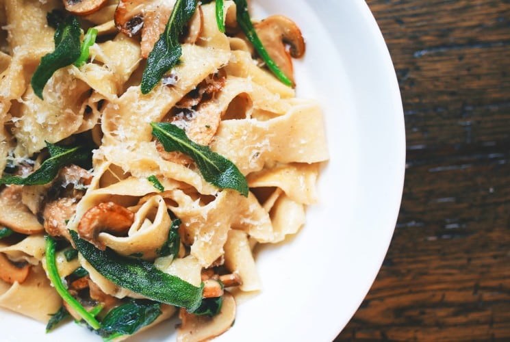 White round plate with pasta and greens on a wood table