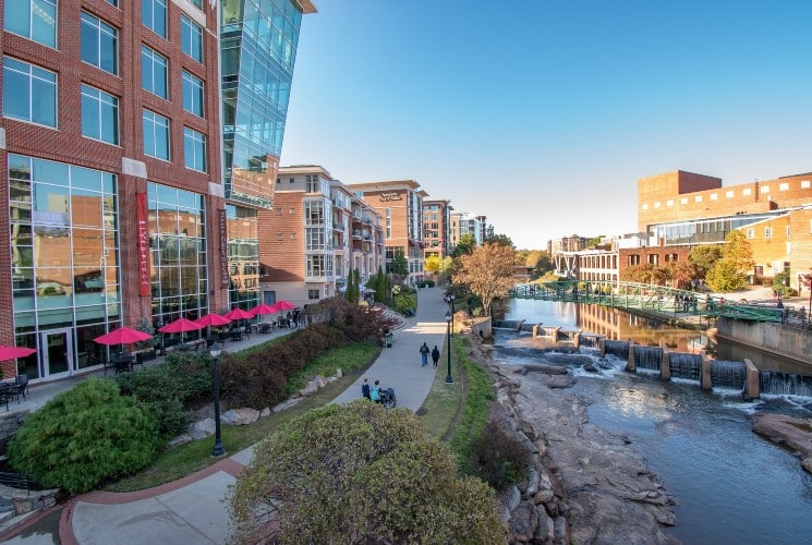 A downtown city center with a walking path next to a river with some cascading waterfalls