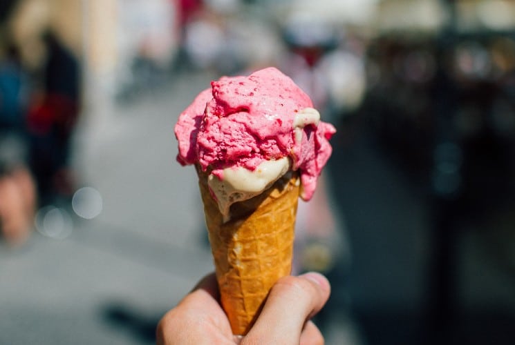 A person holding an waffle ice cream cone with pink ice cream