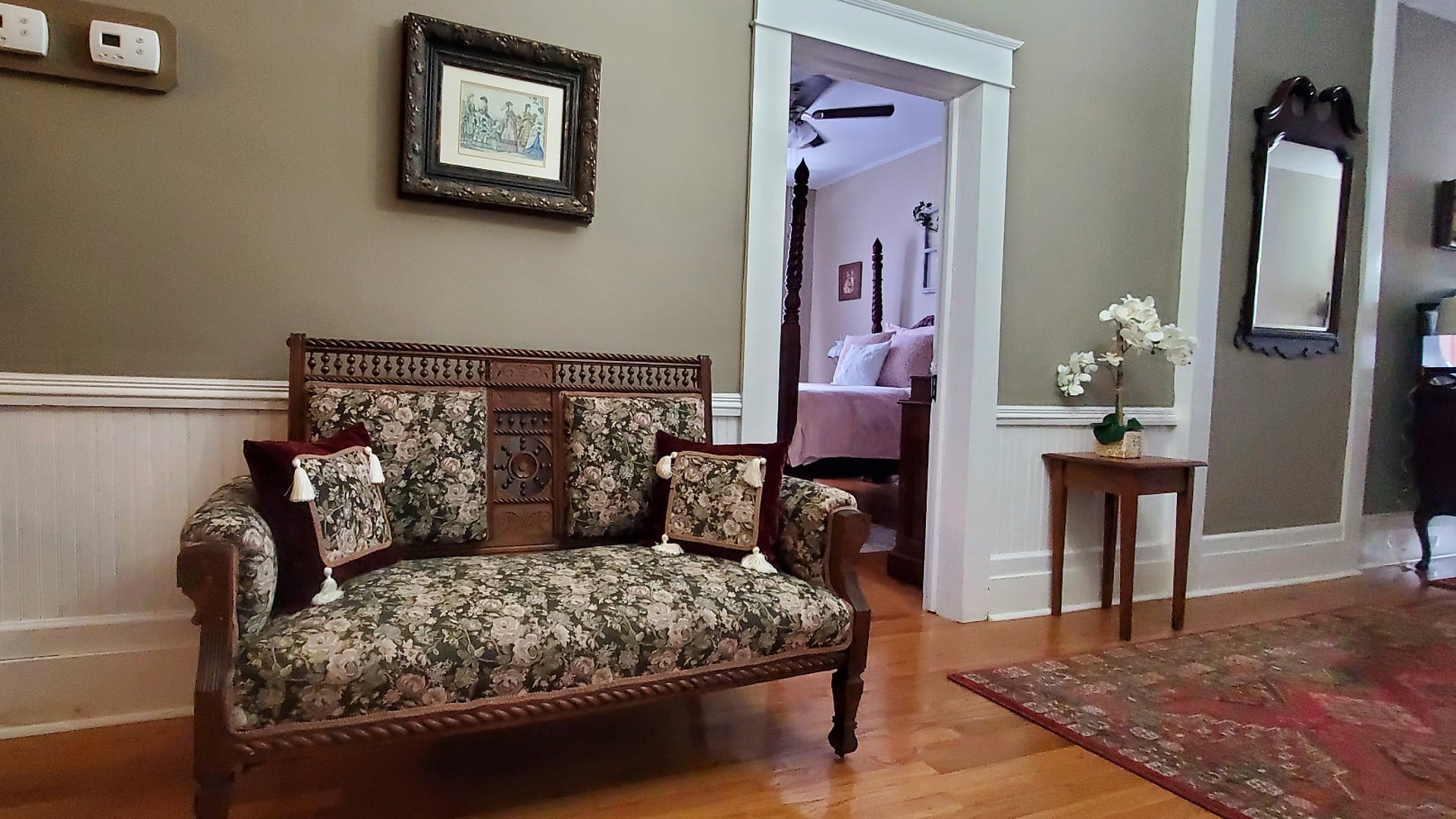Hallway of a home with an antique loveseat in a floral pattern next to a doorway to a bedroom