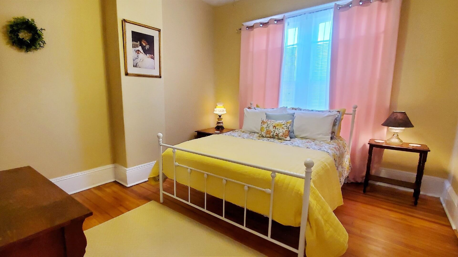 Quaint bedroom with white wrought iron headboard and footboard, yellow walls and window with pink curtains