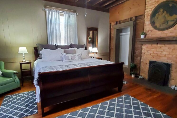 Cozy bedroom with sleigh bed in white and grey, green sitting chair and stone fireplace