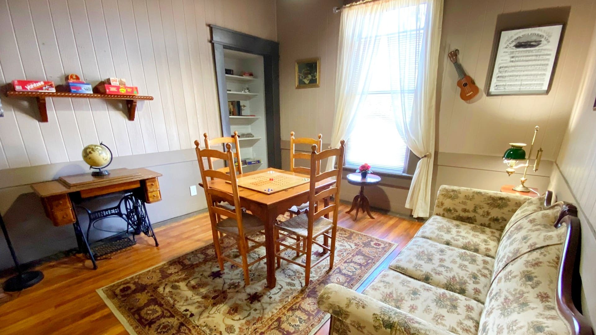 A small room with couch, table with four chairs, built in shelving, antique sewing table and large window