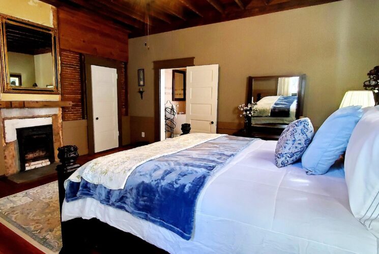 Spacious bedroom with queen bed in white and blue linens, fireplace and doorway into a bathroom