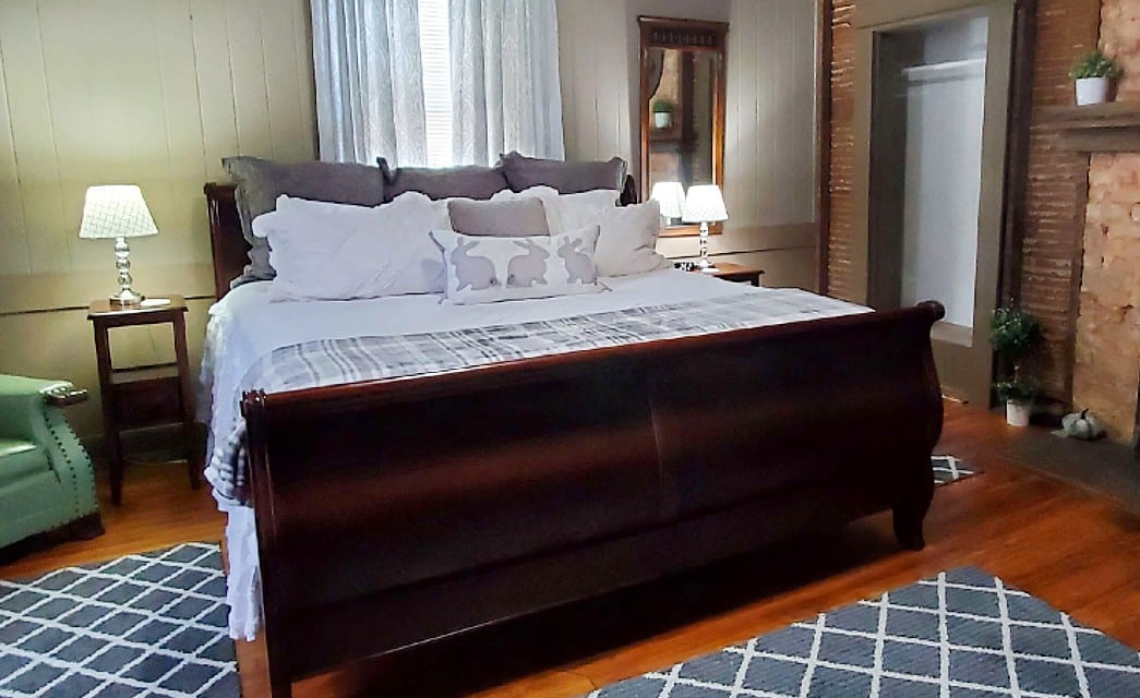 Cozy bedroom with sleigh bed in white and grey, green sitting chair and stone fireplace