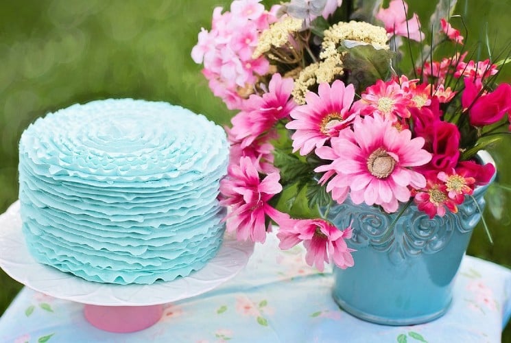 A small outdoor table with a blue cake and vase of pink flowers