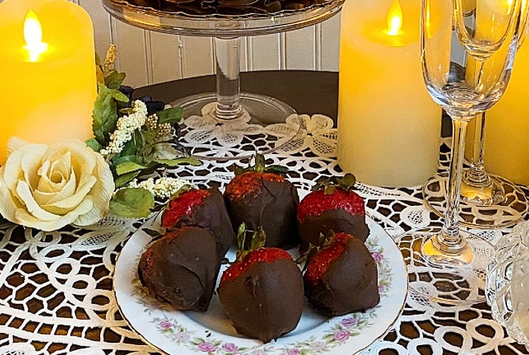 Table set with candles, chocolate cake, chocolate dipped strawberries, and bottle of cider with two flutes
